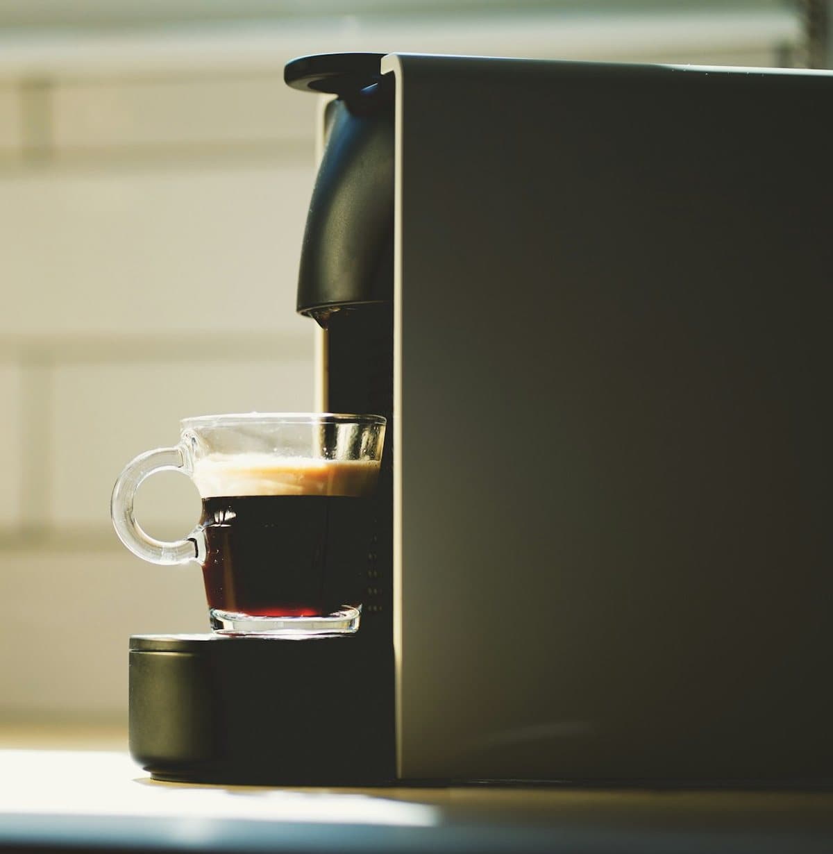 Espressor cu capsule care prepară un espresso într-o ceașcă de sticlă, în lumina caldă a dimineții