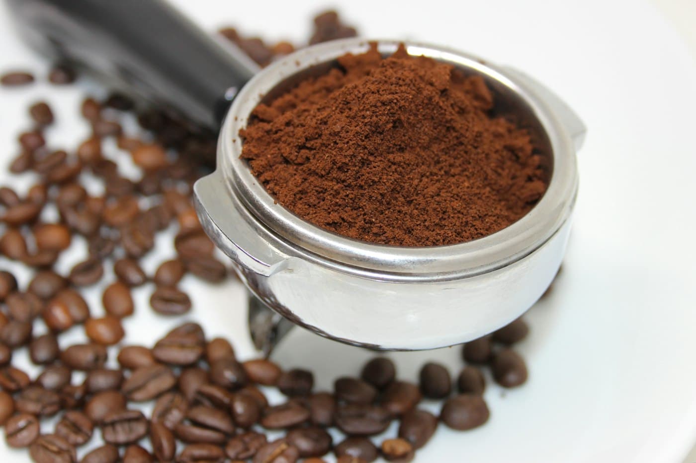 Portafiltru cu cafea măcinată, lângă boabe